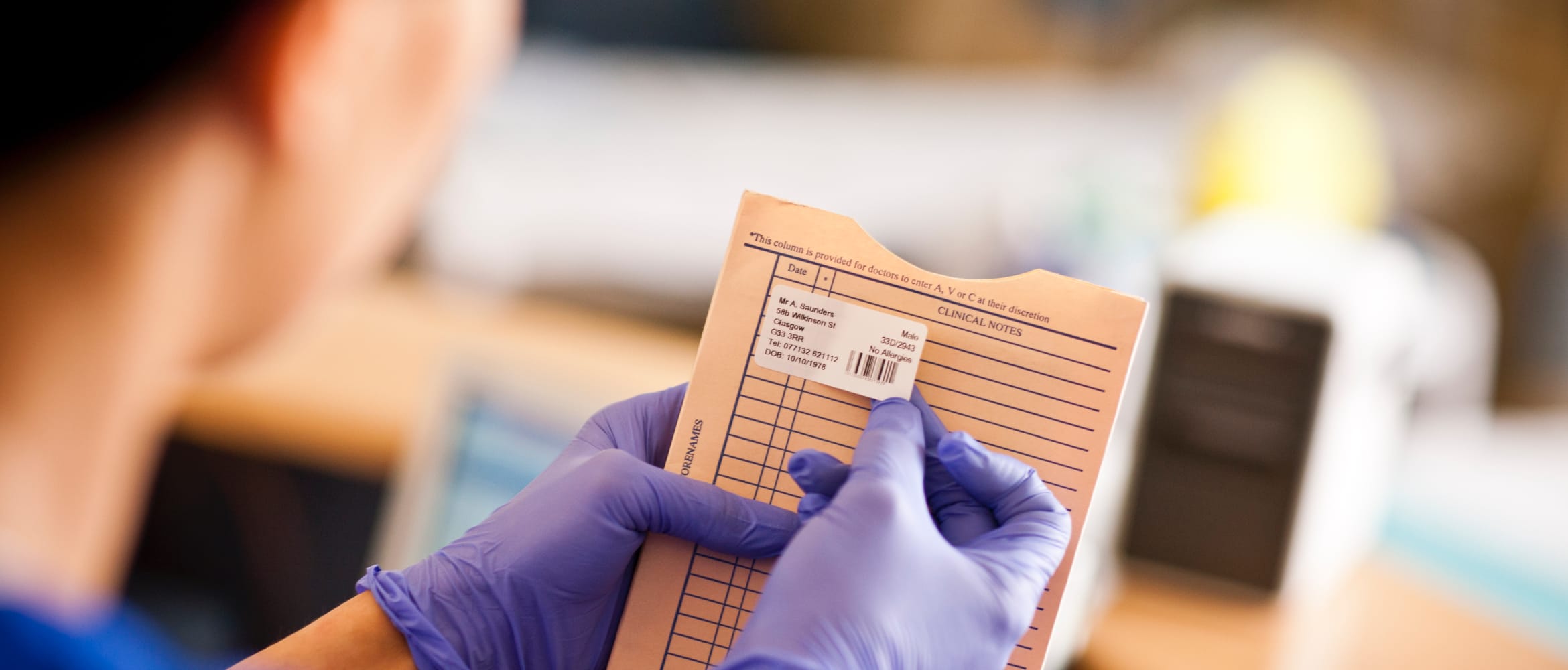 Medical professional wearing purple gloves applying printed label to patients clinical notes