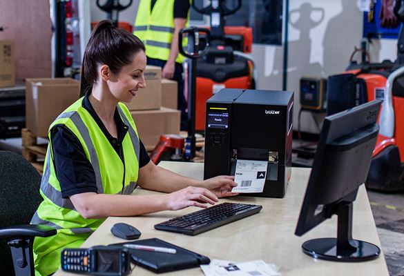 Warehouse worker in high vis vest sat at desk printing from Brother industrial label printer