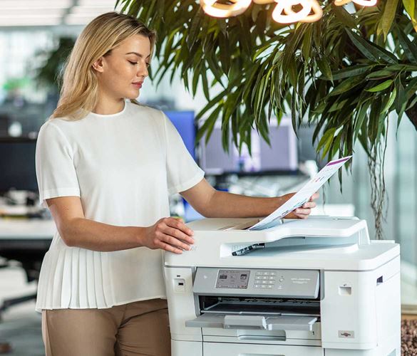 Woman stood next to a Brother printer looking at her newly printed document