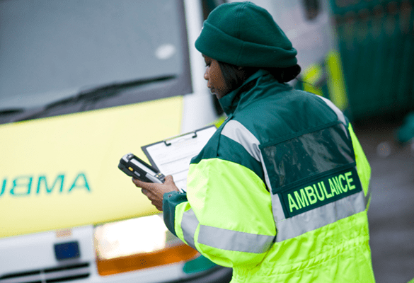 An emergency worker looking at a mobile device with an ambulance in the background