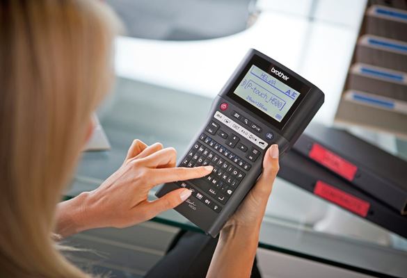 A lady using a PT-H500 professional handheld label printer while sat at a glass table with ring binders in the background