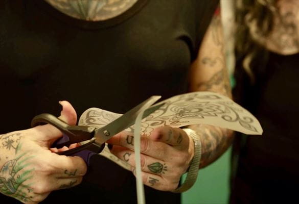 A tattoo artist using scissors to cut around a printed stencil