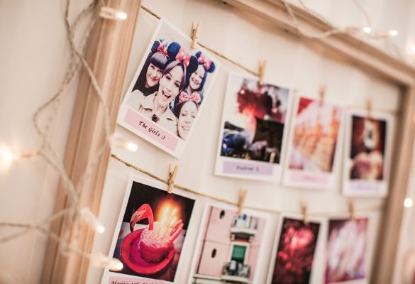 Photographs printed in a polaroid format pegged to lines of string within a picture frame with fairy lights around the edge