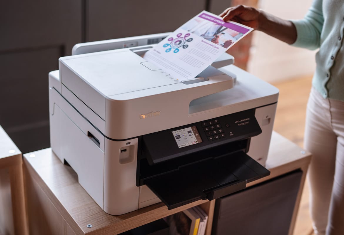 A lady feeding a colour document into the top document feeder of a wireless all-in-one printer which is sat on a wooden shelving unit