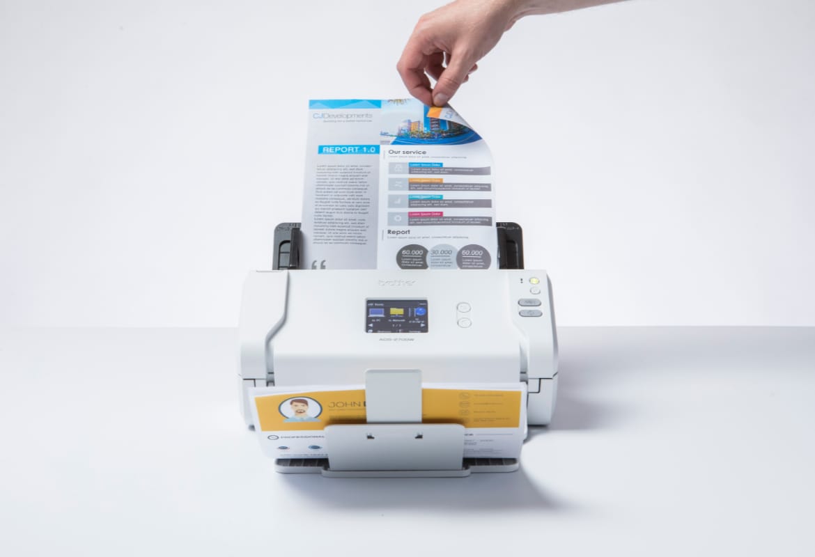 A person who is out of shot turning the page of a double-sided document in the input tray of Brother ADS-2700W sheetfed scanner