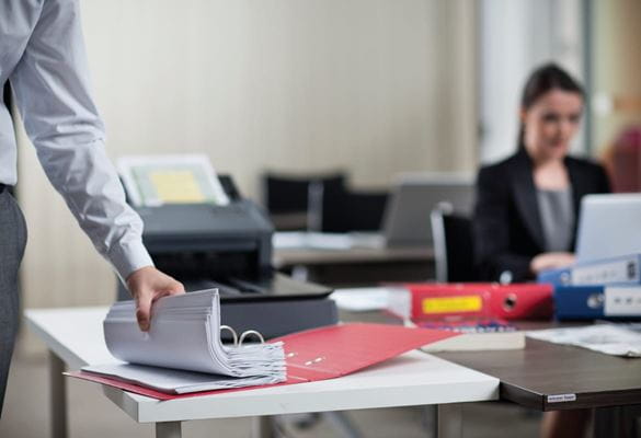 A person leafing through a stack of documents in an office environment with a Brother multiple page scanner in the background