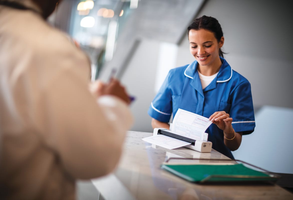 A female healthcare professional using a portable Brother scanner at a reception desk to scan patient notes