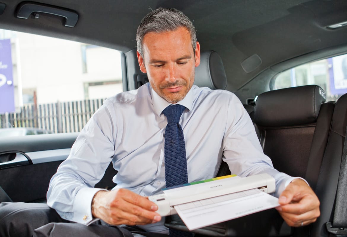 A businessman using a portable wireless scanner while sat in the back seat of a stationary vehicle