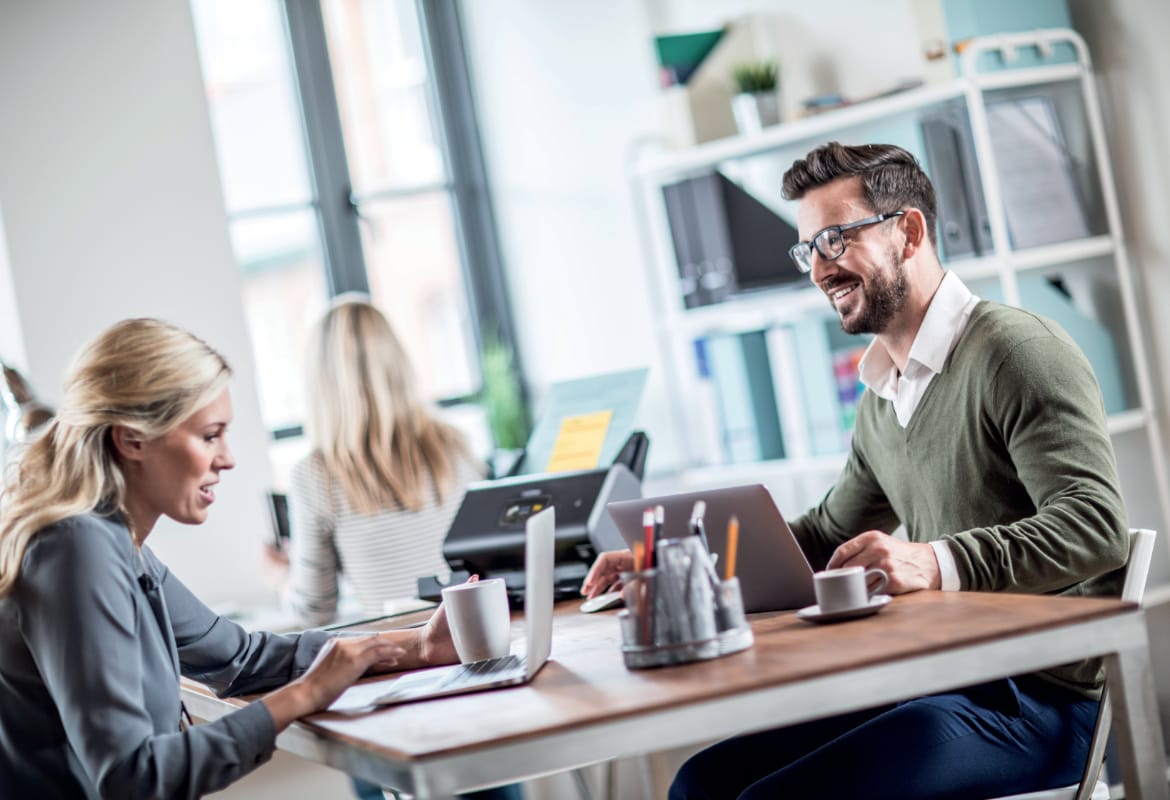 Male and female colleagues sat at a desk in a small office environment with a Brother wireless scanner and another female colleague in the background