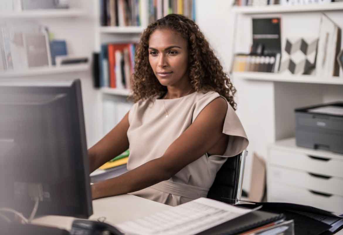 Lady sat in her home office working on a computer with a Brother printer in the background