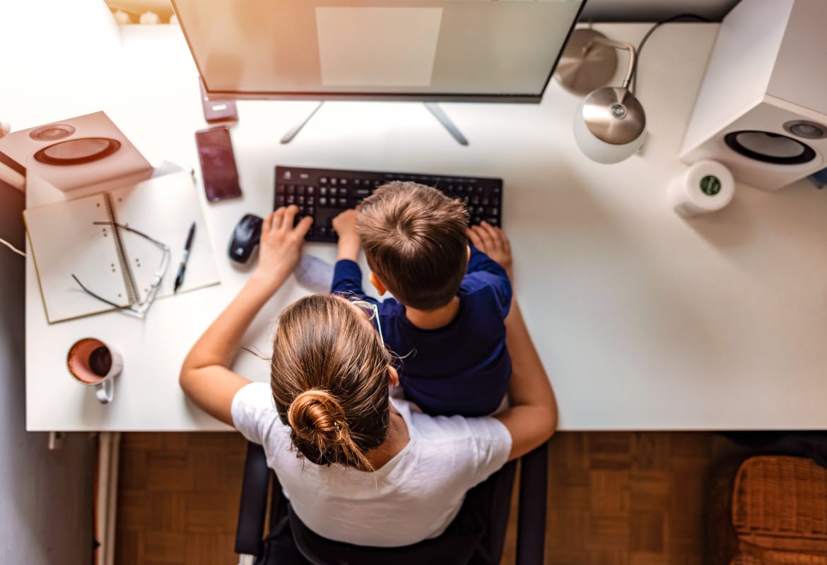 Overhead view of a young mother working on a desktop computer with her son sitting in her lap in a home office environment