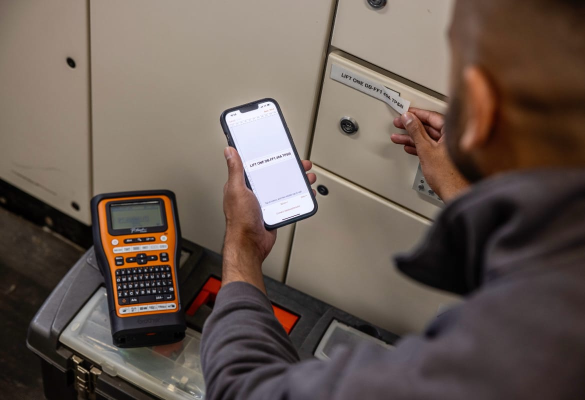 An electrician using Brother's Pro Label Tool app on a smartphone to print to a handheld label printer