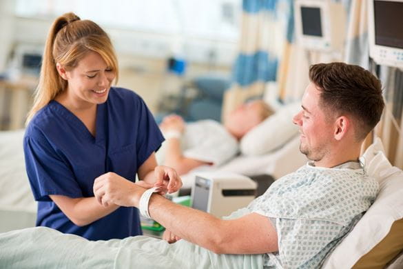 Nurse fastening a wristband to a patient lying in a hospital bed