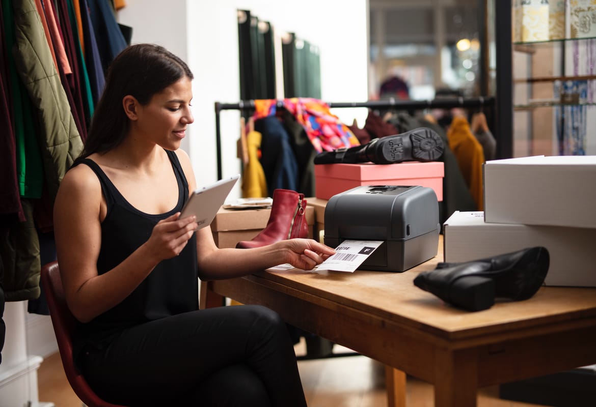 A sales assistant printing a barcode label for a customer order at the back of a high street fashion retail store