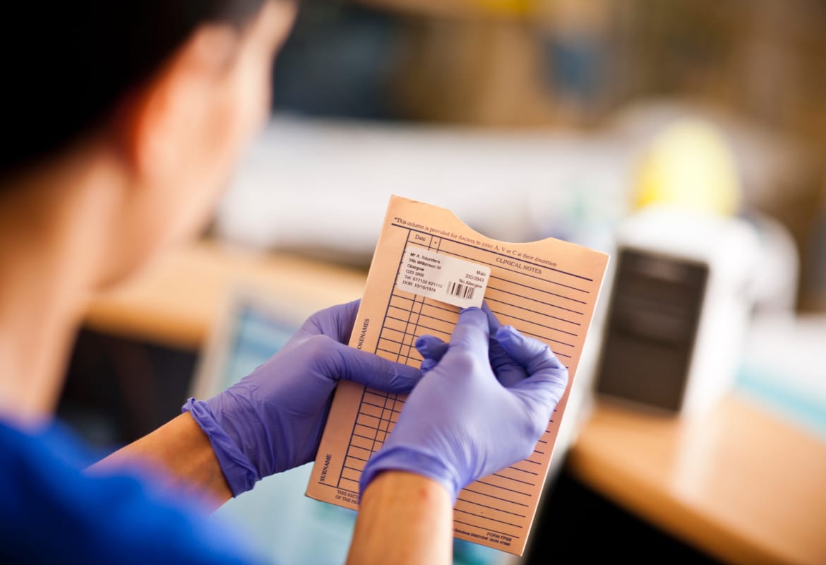 Medical professional wearing purple gloves applying printed label to patients clinical notes