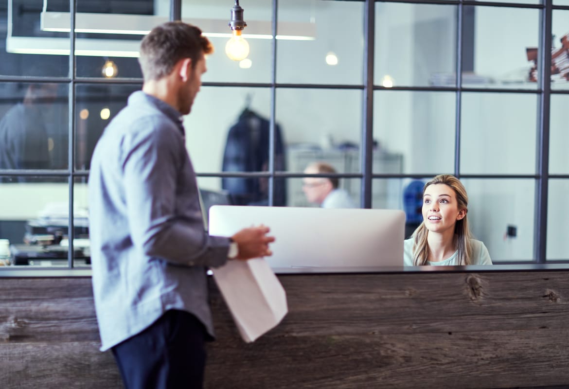 Female store staff member sat behind at a customer service desk talking to a male customer