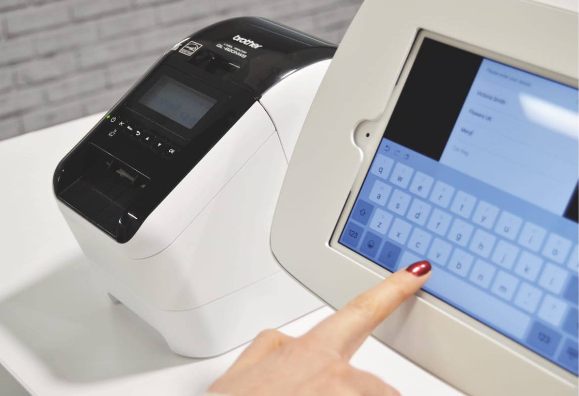 A lady entering information into a visitor management system which is on a table next to a Brother QL-800 series label printer