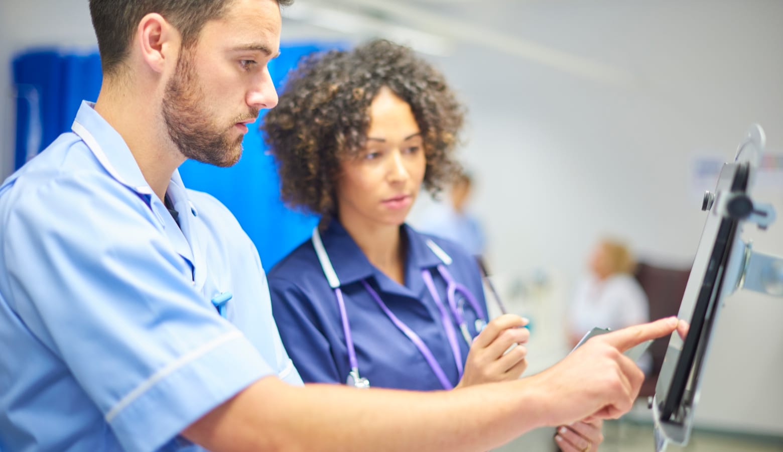 Male nurse checking information on a tablet device while being supervised by a female staff nurse