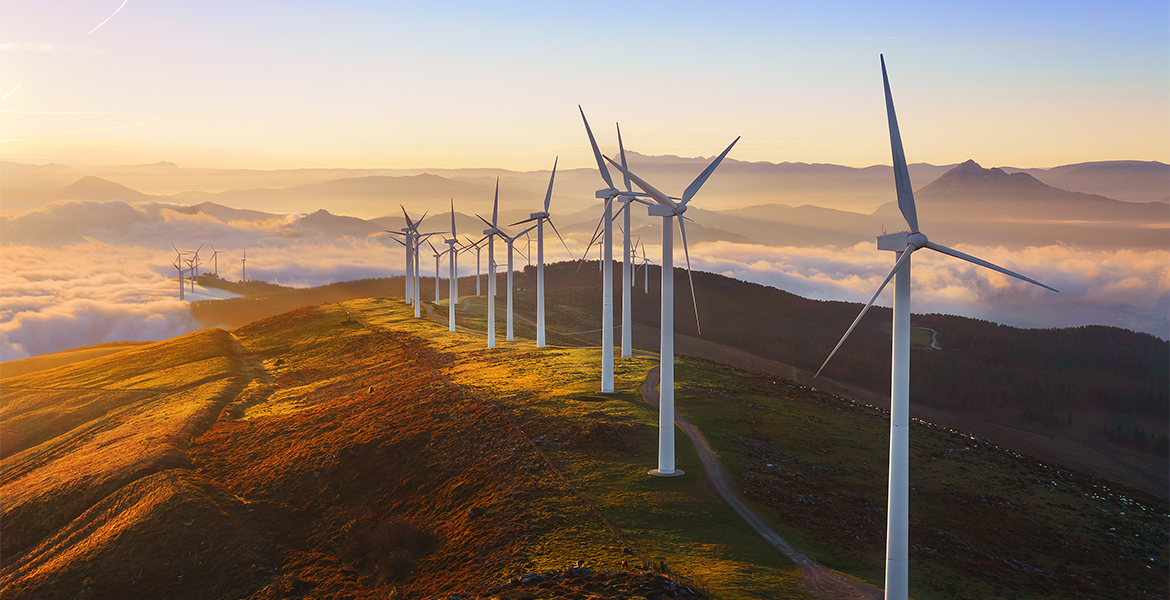 Series of wind turbines on a green hill with blue sky and clouds