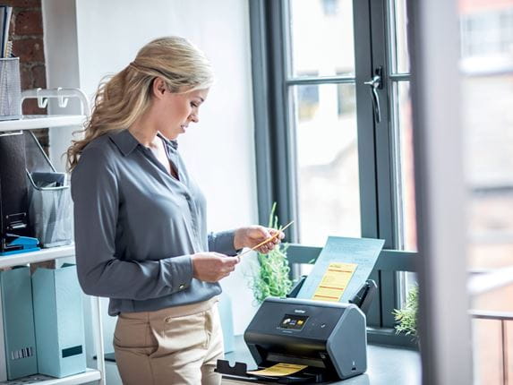 Business woman using a Brother ADS-2800W to scan documents in front of a window in an office environment