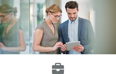 A business woman and business man looking at a tablet device in front of a glass panelled office building
