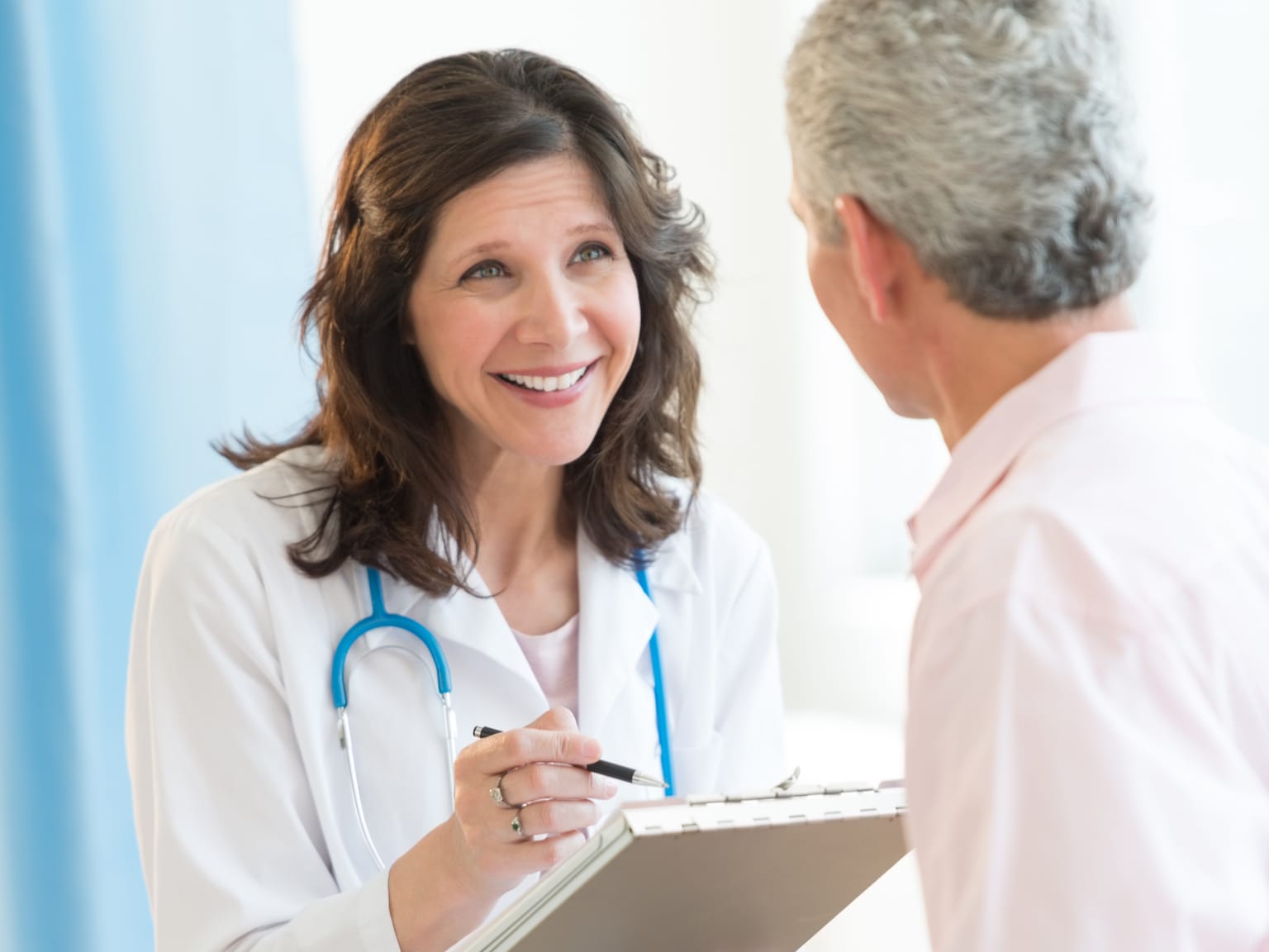 Female doctor taking notes while talking to a male patient in a surgery environment