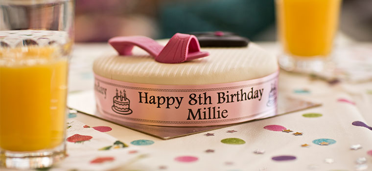 Iced birthday cake with ribbon around on table with spotty table cloth, orange juice, glasses