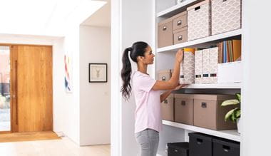 A lady pulling a labelled box file from a bookshelf in a home office environment