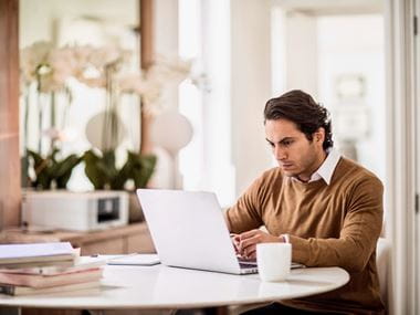 A man looking concerned reading an email on his notebook computer while sat at a table in a home working environment