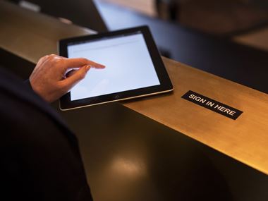 Close-up of a person using a tablet device to sign in at a reception desk