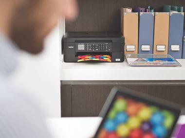 A person wirelessly printing a colourful image from an iPad to a Brother inkjet printer