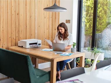 A lady checking a printer colour test page while sat at a table in a home working environment