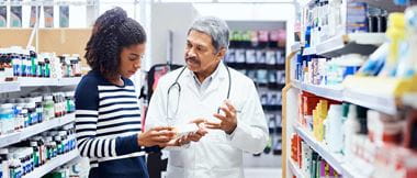 a pharmacist offers help to a woman in the aisle of a pharmacy