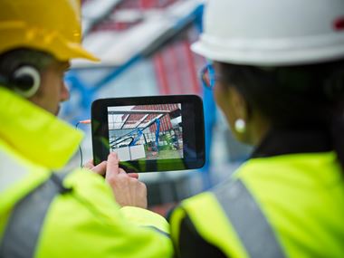 Two construction workers taking a photograph on site with a tablet device