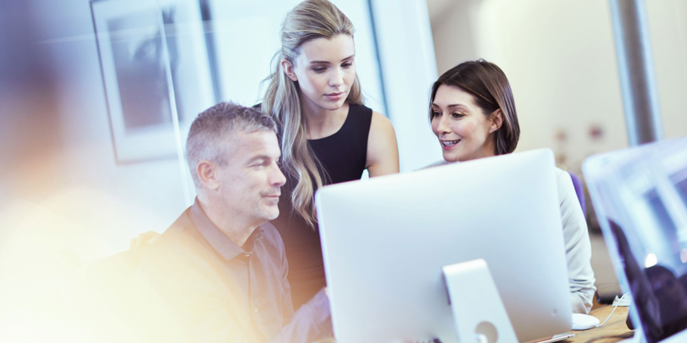 Three colleagues looking at a computer monitor in an office environment
