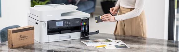 Woman stood at table putting a cartridge into a printer with a box next to it and sofa and pictures in background
