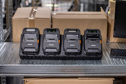 Four Brother RJ-3200 rugged printers on PA4CR003 4-bay charging cradle in warehouse