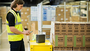 Man wearing a high visibility vest in a warehouse printing a label from a smartphone