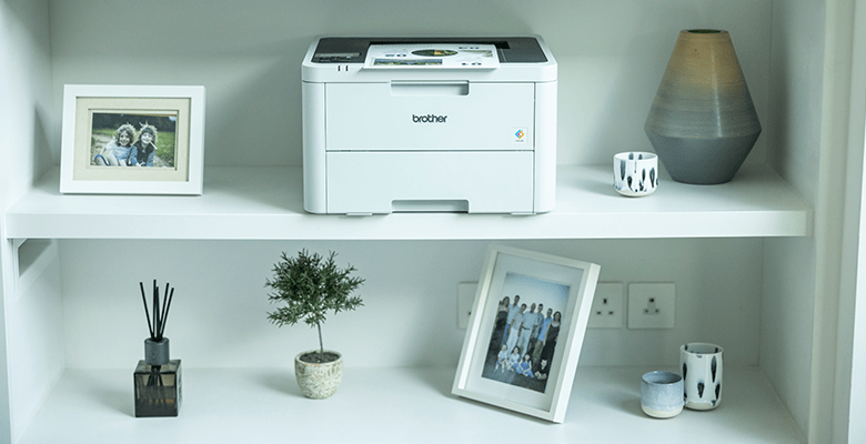 A printer on a shelf surrounded by framed photographs and decorative ornaments