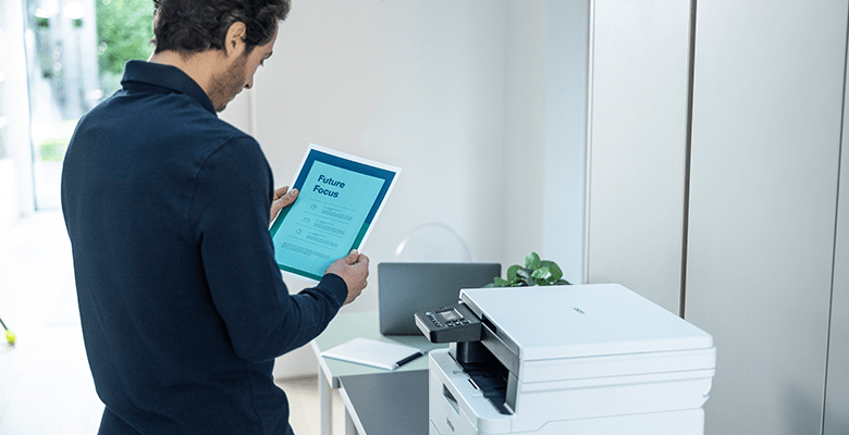 A man reading a document while stood next to a printer in an SMB environment