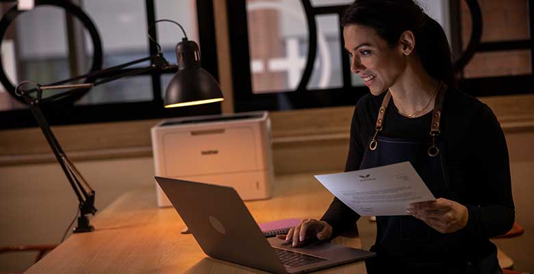 Female sat in the dark holding document, laptop, window
