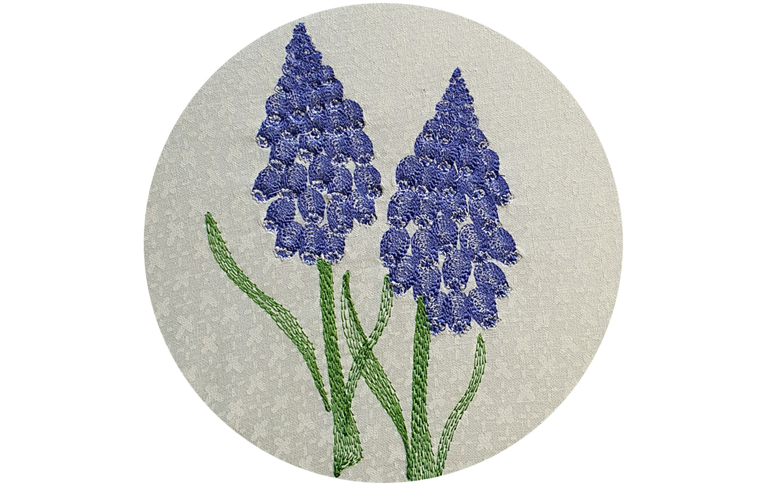 Two purple embroidered muskari flowers on white fabric