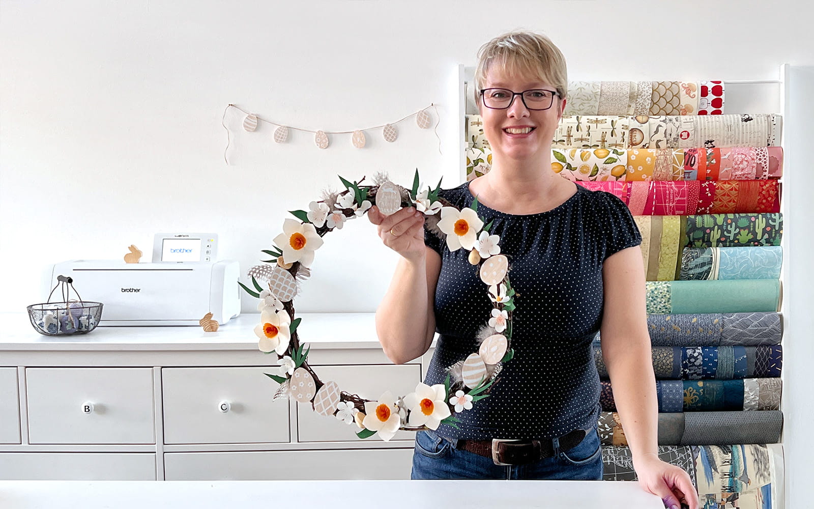 blonde woman holds floral papercraft wreath in craft room
