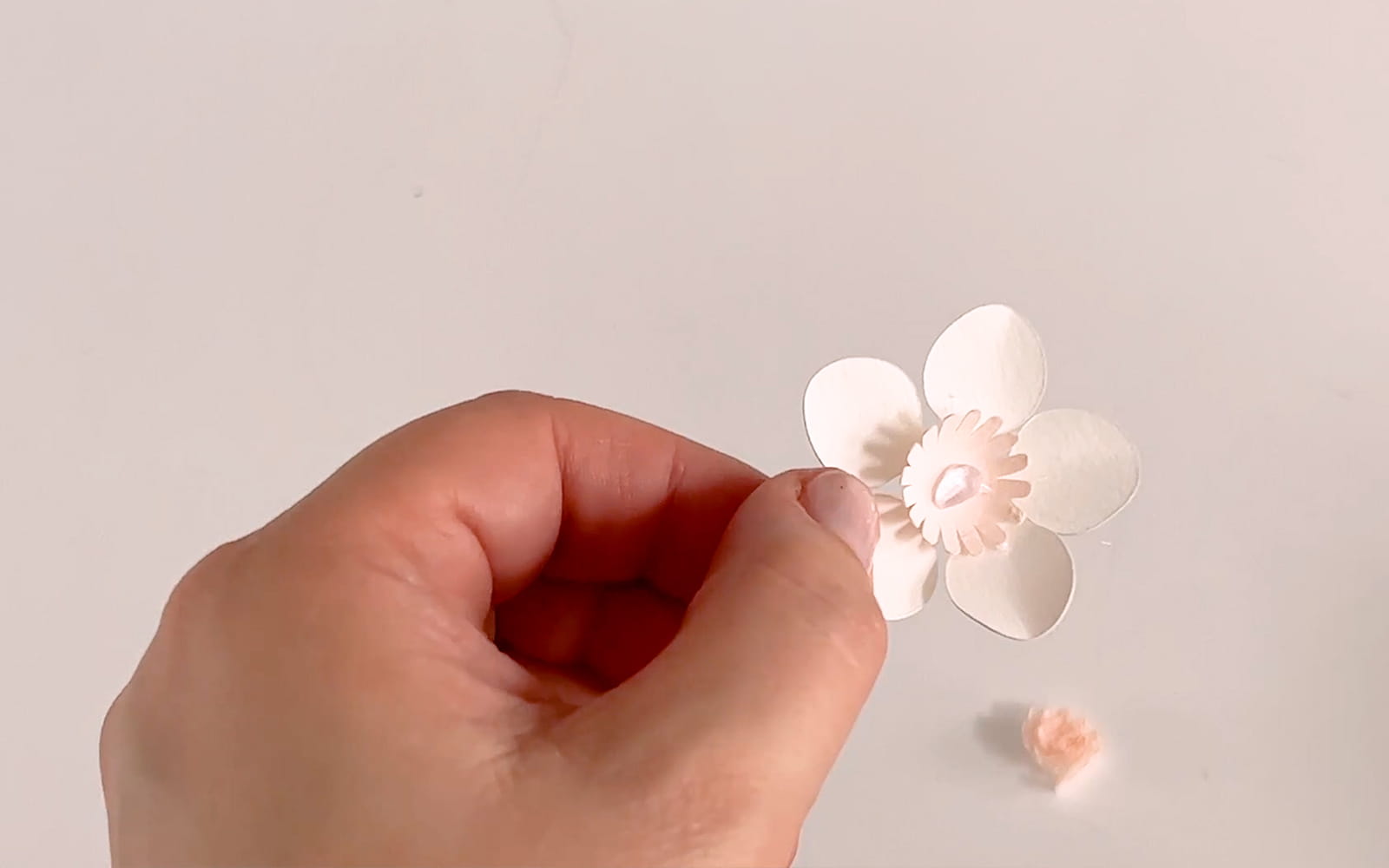Eine Hand hält eine weiße und hellrosa Pappmaché-Kirschblüte