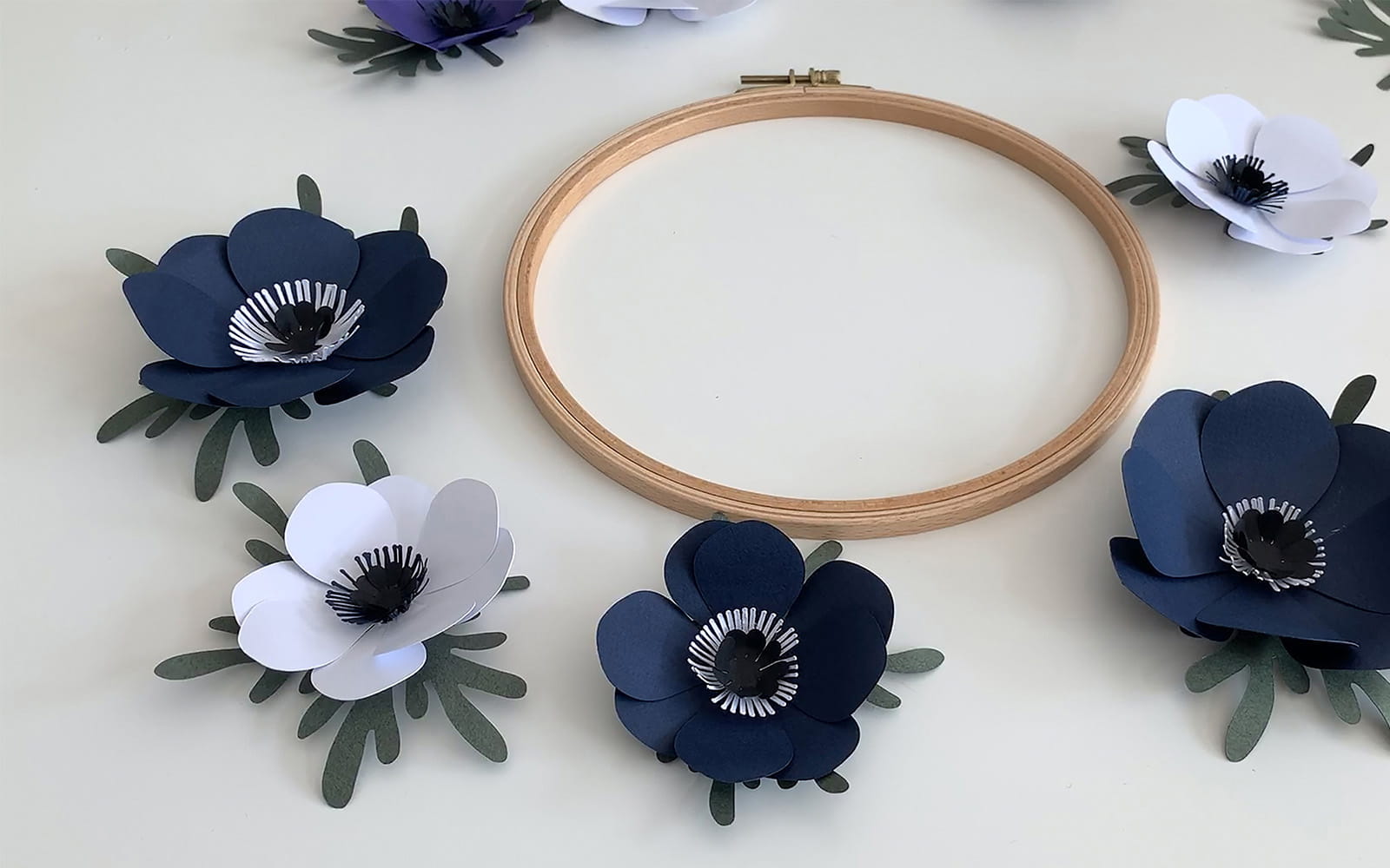 A wooden embroidery hoop with blue and white paper flowers around
