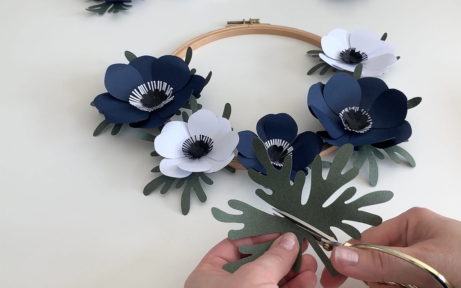 Hands cutting a green paper leaf to stick on embroidery frame wreath