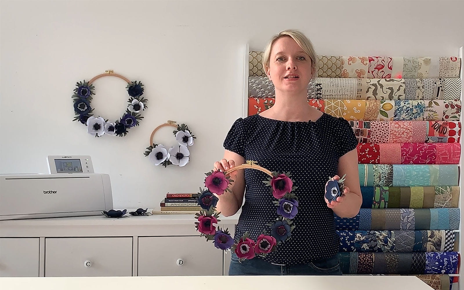 Blonde haired woman standing in craft room with paper flower wreath