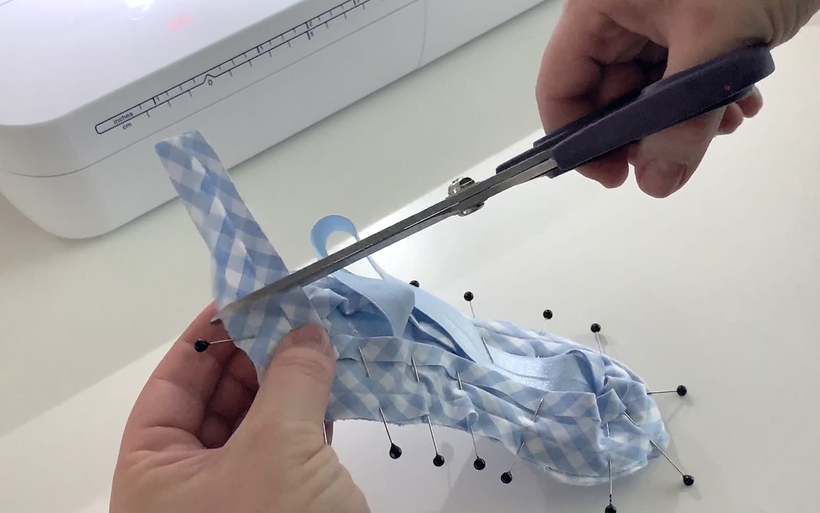 hands using scissors to cut down end of blue check bias tape