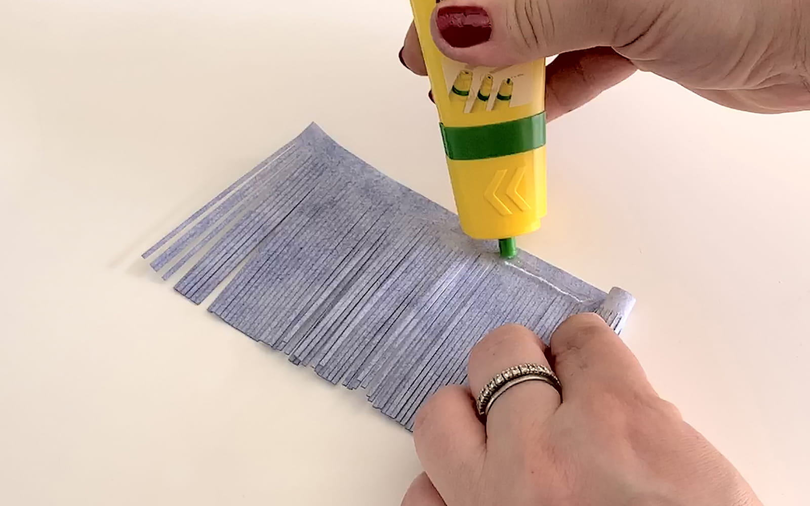 Yellow tube of liquid glue being squeezed onto blue tassel
