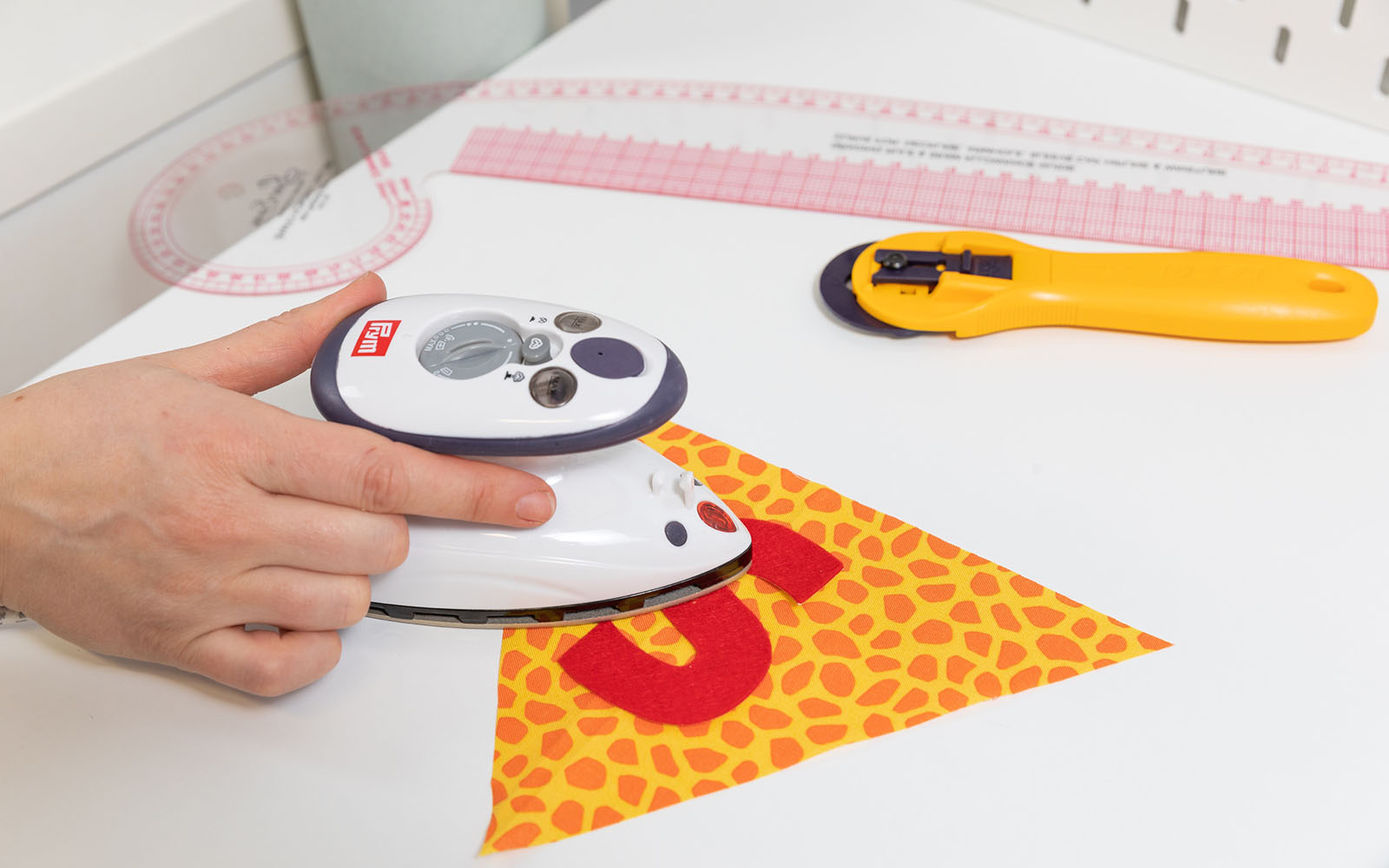 Hand holding small iron ironing applique letter onto bunting